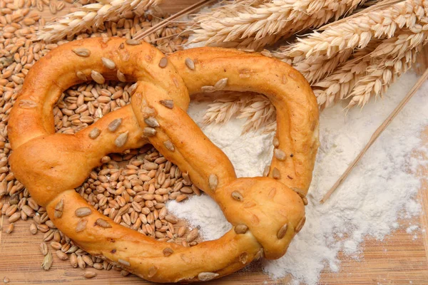 Grani, spighe di grano, farina e pretzel su un tavolo di legno. Concetto — Foto Stock