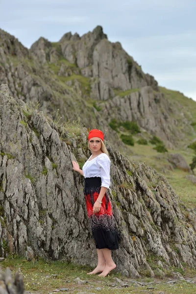 Hermosa mujer rubia sentada descalza junto a una roca al atardecer —  Fotos de Stock
