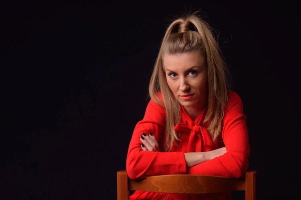 Beautiful blonde young woman in a red dress is sitting on a chai — Stock Photo, Image