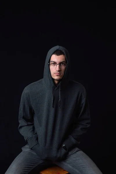 Zelfverzekerde jonge man dragen van bril en zwarte hoodie poseren op een — Stockfoto