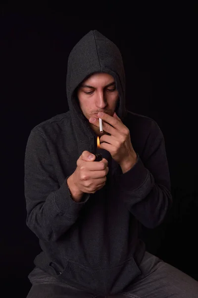 Teenager in a hooded sweatshirt lights a cigarette with lighter — Stock Photo, Image