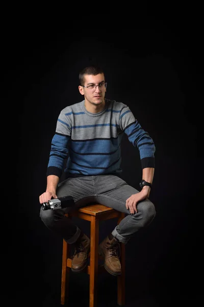 Joven hombre de pie en una silla y la celebración de la vieja cámara en bac oscuro —  Fotos de Stock