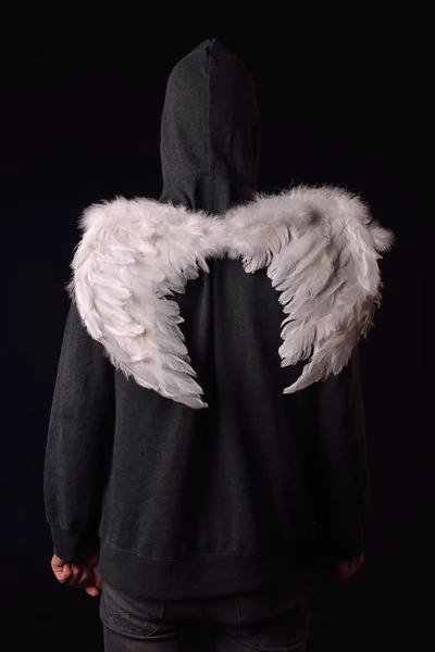 На спине молодого человека с черной толстовкой и белыми пернатыми крыльями — стоковое фото