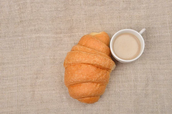 黄油羊角面包和一杯咖啡加牛奶附近黄麻 b 上 — 图库照片