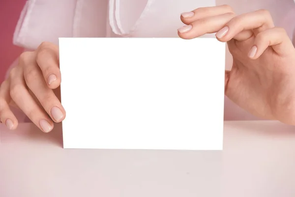 Närbild kvinnlig hand på en rosa bakgrund håller ett tomt ark för att fylla — Stockfoto