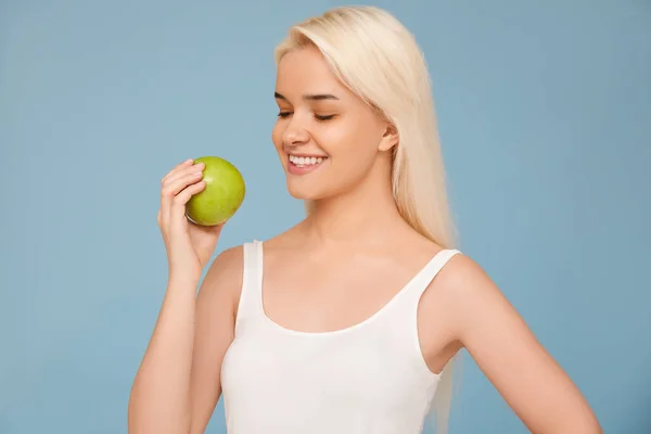 Kvinna med äpple. Vacker flicka med vitt leende på en blå bakgrund, friska tänder. Högupplöst bild — Stockfoto
