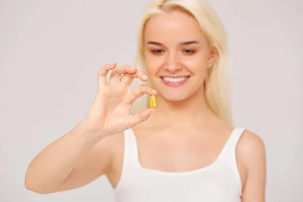 Mulher sorridente bonita segurando pílulas de óleo de peixe em sua mão em um fundo cinza. Alimentação saudável — Fotografia de Stock