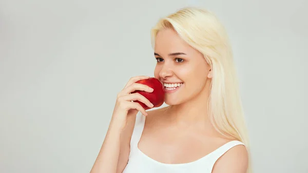 Kvinna med äpple. Vacker flicka med vitt leende på en grå bakgrund, friska tänder. Högupplöst bild — Stockfoto