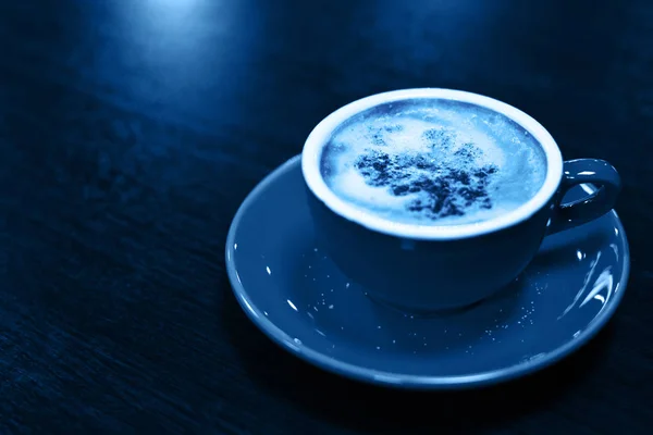 올해의 색깔, 2020 년. 나무 배경에 카푸치노나 라떼를 탄 커피 잔에는 전형적 인 파란색 사진이 담겨져 있다. 커피 잔, 맨 위 사진. — 스톡 사진