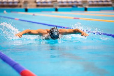 Yüzme havuzunda açık mavi suyla kelebek gibi yüzen atletik bir adam..