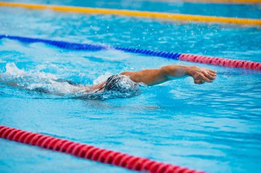 Yüzme havuzunda temiz mavi suyla yüzen atletik bir adam..