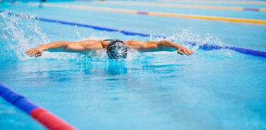 Yüzme havuzunda açık mavi suyla kelebek gibi yüzen atletik bir adam..