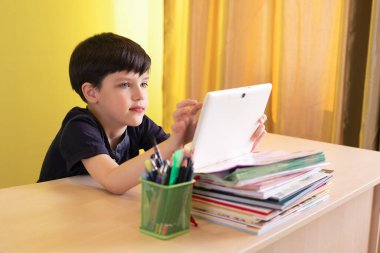 Koronavirüs karantinası sırasında çocuk ödevlerini yaparken tableti kullanıyor. Uzaktan eğitim kavramı.