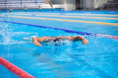 Yüzme havuzunda açık mavi suyla kelebek gibi yüzen atletik bir adam..