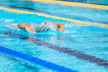 Yüzme havuzunda açık mavi suyla kelebek gibi yüzen atletik bir adam..