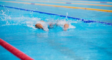 Yüzme havuzunda açık mavi suyla kelebek gibi yüzen atletik bir adam..