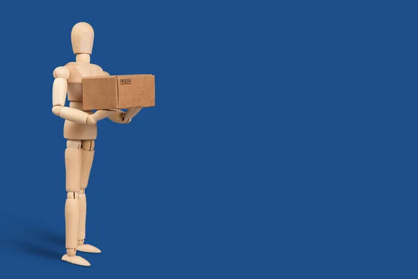 Toy man, delivery service worker with a cardboard box in his hands. Blue classic background. Delivery and Shipping Services Concept.