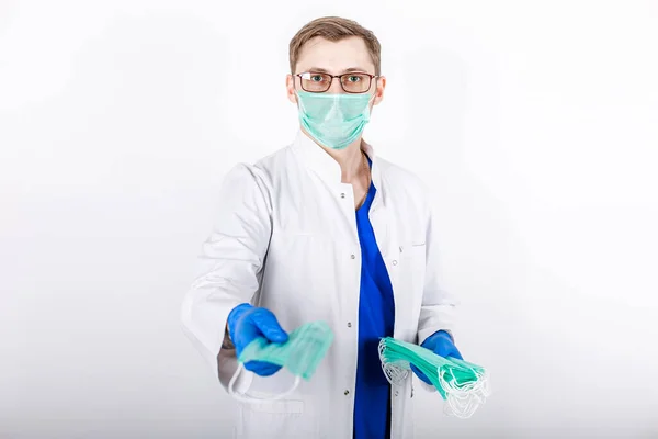 Doktor koruyucu maskeler veriyor. Beyaz arka plan. Özel koruma altında bir sağlık görevlisi, beyaz önlük, eldivenler ve maske. Halk için koruyucu maske. COVID-19