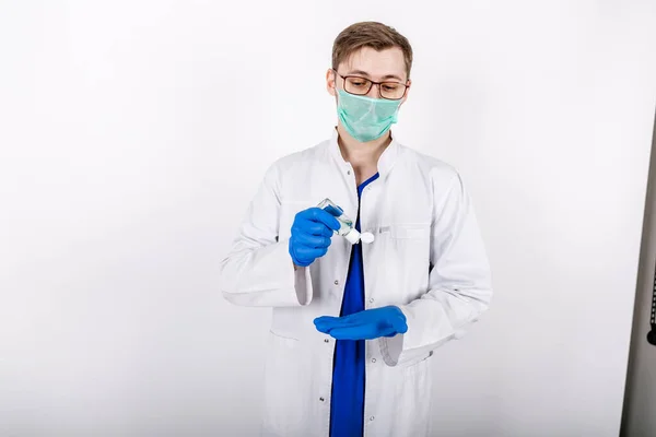 Doktor mavi eldivenli bir antiseptik kullanır. Beyaz önlüklü ve koruyucu eldivenli bir doktor. Eldivenli dezenfektan kullanımı. Beyaz arka plan. Hijyen ürünleri. COVID-19 Koruma