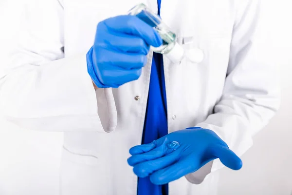 The doctor uses an antiseptic with blue gloves. Doctor in a white coat and protective gloves. The use of a disinfectant with gloves. White background. Hygiene product. COVID-19 Protection