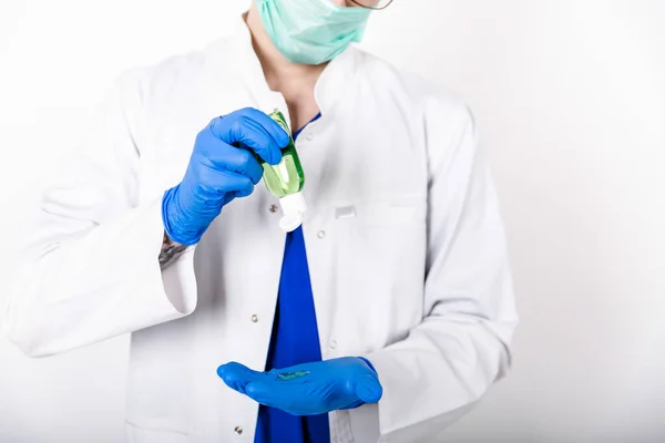 The doctor uses an antiseptic with blue gloves. Doctor in a white coat and protective gloves. The use of a disinfectant with gloves. White background. Hygiene product. COVID-19 Protection