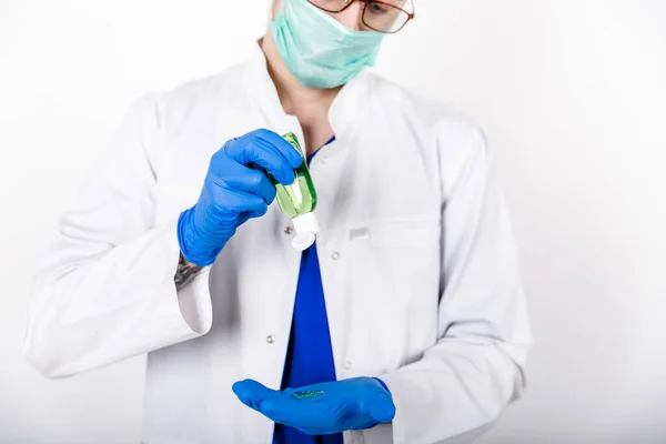 Doktor mavi eldivenli bir antiseptik kullanır. Beyaz önlüklü ve koruyucu eldivenli bir doktor. Eldivenli dezenfektan kullanımı. Beyaz arka plan. Hijyen ürünleri. COVID-19 Koruma