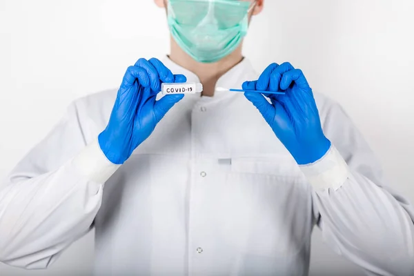 Bir sağlık uzmanı COVID-19 lekesi alır. Beyaz bir bornoz giy, koruyucu bir maskeden yapılmış eldivenler giy. Analiz için test tüpü. Analiz ve enfeksiyon örneği için test tüpü olan bir doktor..