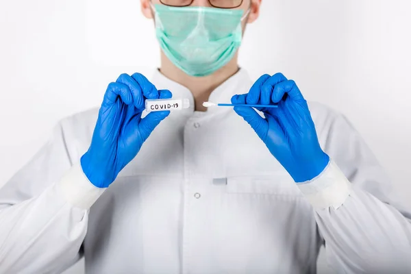 Bir sağlık uzmanı COVID-19 lekesi alır. Beyaz bir bornoz giy, koruyucu bir maskeden yapılmış eldivenler giy. Analiz için test tüpü. Analiz ve enfeksiyon örneği için test tüpü olan bir doktor..