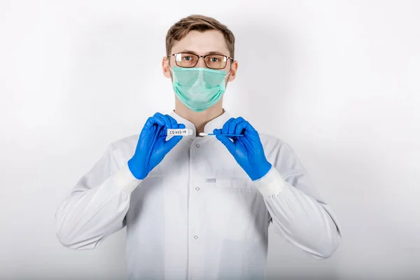 Bir sağlık uzmanı COVID-19 lekesi alır. Beyaz bir bornoz giy, koruyucu bir maskeden yapılmış eldivenler giy. Analiz için test tüpü. Analiz ve enfeksiyon örneği için test tüpü olan bir doktor..