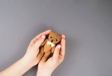 Manikürlü, gri arka plan manzaralı oyuncak ayılı bir kızın elleri.