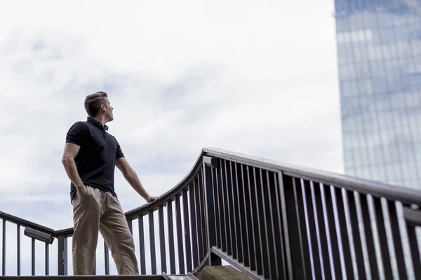 Hombre parado en una escalera al aire libre y mirando un rascacielos —  Fotos de Stock