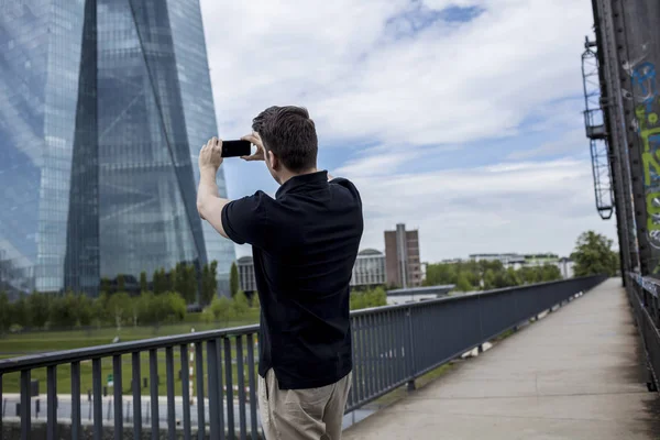 Homem na ponte fotografando edifício arranha-céu — Fotografia de Stock