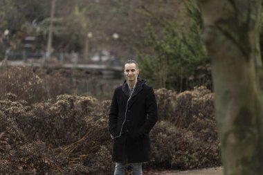 Sonbaharda halka açık parkta poz veren kulaklıklı beyaz bir genç. Üç çeyrek uzunluk.