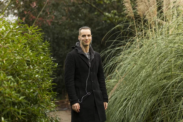 植物園でイヤホンと黒のコートのポーズを持つ男 — ストック写真