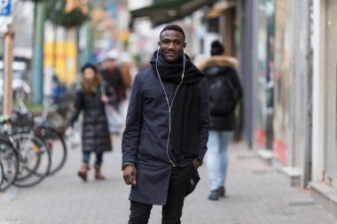 Genç siyahi adam, bir eli cebinde, kaldırımda duran kulaklıkları dinliyor..