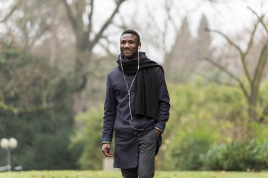 Genç siyahi bir adam güvenli bir şekilde parkta yürüyor ve başka tarafa bakıyor..