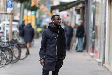 Elleri cebinde, kulaklıkları kaldırımda başı dönük duran genç siyah bir adam..