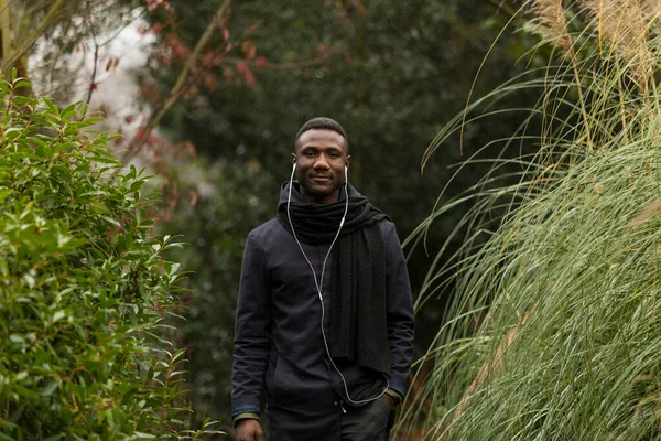 Joven Hombre Negro Escuchando Auriculares Posando Parque Mirando Cámara — Foto de Stock