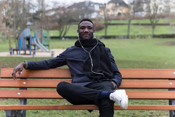 Joven Hombre Negro Escuchando Audiolibro Sentado Banco Del Parque Mirando —  Fotos de Stock