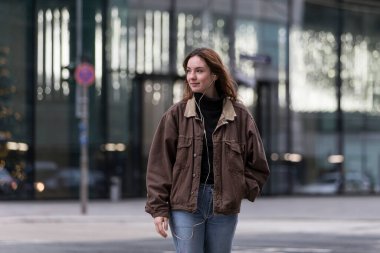 Şehir caddesinde kulaklık dinleyen genç bir kadın başını kameraya çevirmiş..