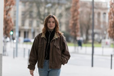 Ceketinin cebinde kameraya bakan beyaz bir kadın. Şehir sokağı geçmişi.