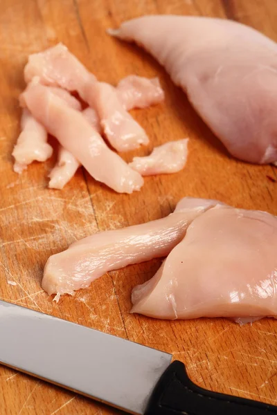 Cutting chicken breast into strips on wooden kitchen board