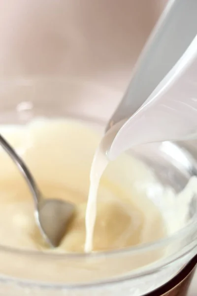 Pouring milk into melted white chocolate. Making frozen strawberry cheesecake series.