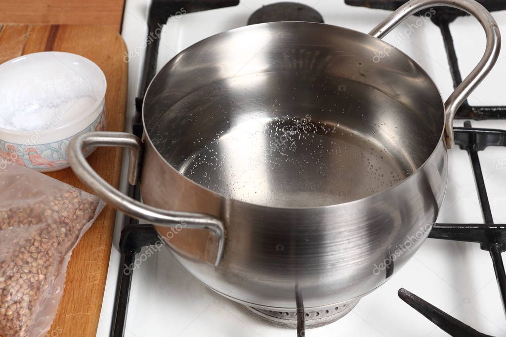 Boiling water into saucepan. Cooking buckwheat groats on gas stove.