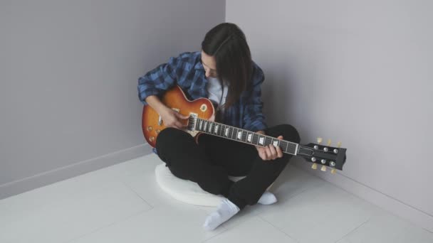 아름다운 여성이고 전자 기타 연주와 락 콘서트 연습을 하고 있습니다. 파란 셔츠를 입고 기타 연주와 노래를 하며 마루에 앉아 있는 여자. — 비디오