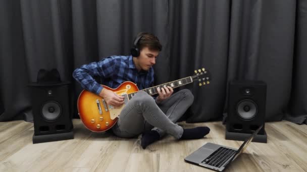 Joven tratando de tocar la guitarra. Enojado macho molesto en auriculares y ropa casual aprendiendo a tocar en la guitarra eléctrica. Hombre practicando la guitarra — Vídeos de Stock