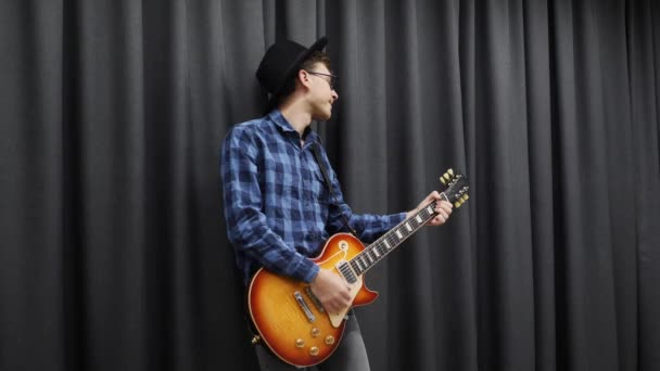 Um homem a tocar guitarra. Jovem menino feliz milenar tocando na guitarra elétrica. O homem do estilo de vida gosta de tocar guitarra. Guitarrista sorridente cantando música na guitarra em estúdio — Vídeo de Stock