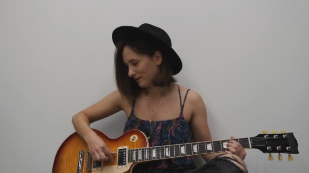 Uma mulher a tocar guitarra. Bonita milenar a tocar instrumentos musicais. Menina de chapéu com maquiagem brilhante tocando na guitarra elétrica — Vídeo de Stock