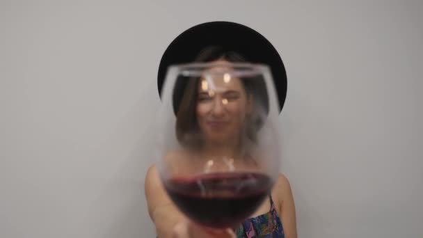 Donna che guarda la telecamera e beve vino. Donna che assaggia vino rosso contro muro bianco. Elegante bella ragazza beve vino rosso — Video Stock