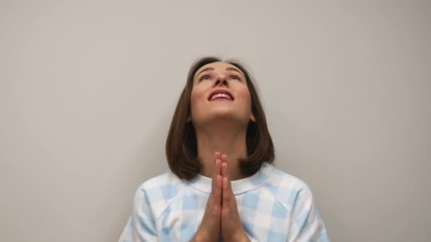 Женщина молится за успешную сделку на белом фоне. Молодая улыбающаяся женщина молится в студии перед камерой — стоковое видео